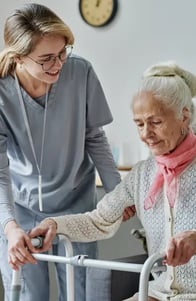 young-caregiver-caring-about-senior-woman-nursing-home-she-helping-her-stand-using-walker 1